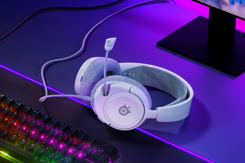An image of Arctis Nova headset laying on the desk, accompanied with glowing keyboard and mouse.