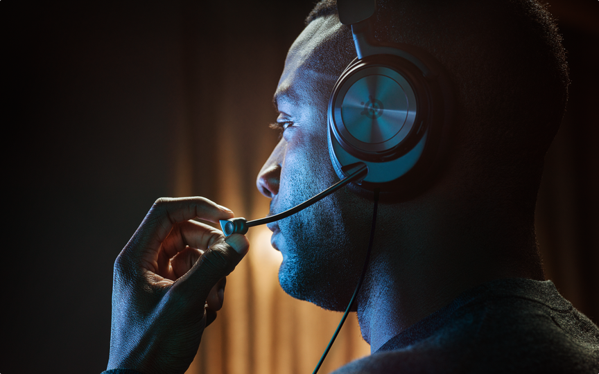 A person sitting with their profile showing off an Arctis Nova gaming headset. They are adjusting the retractable mic.
